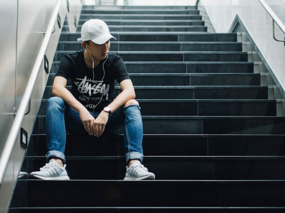 Young man in white baseball cap sits on stairs